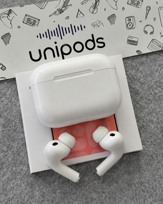 White wireless earbuds in their charging case with two earbuds placed in front, set on a white box with a pink insert. A branded Unipods - Airpods Pro 2  Copy / Clone with ANC card or sheet is visible behind the product on a gray textured surface.