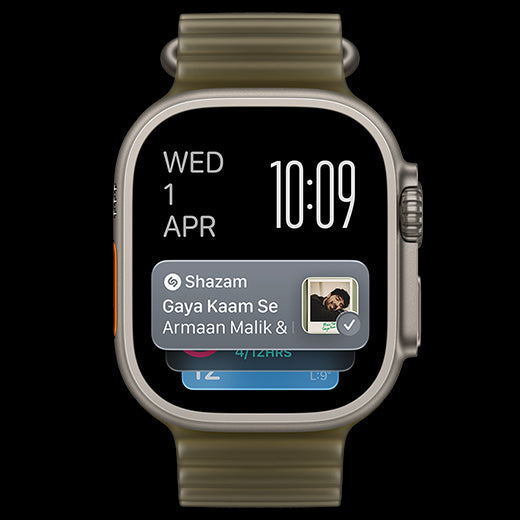 A smartwatch with a metallic silver-toned case and a textured olive green band, shown against a solid black background. The watch face is active with a digital clock showing 10:09 and a notification banner from 'Shazam' displayed on the screen.